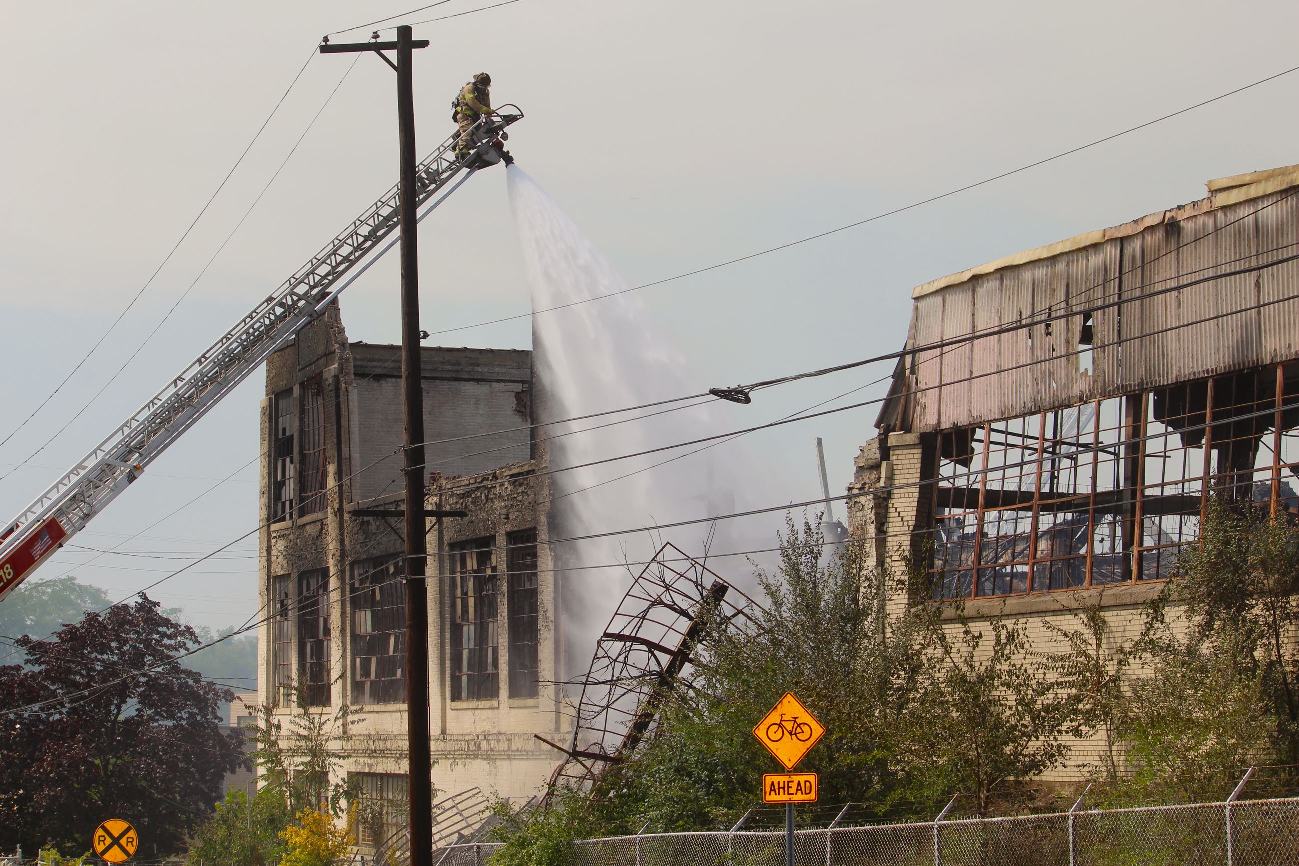 Firefighter sprays water from a ladder on a fire damaged brick building 