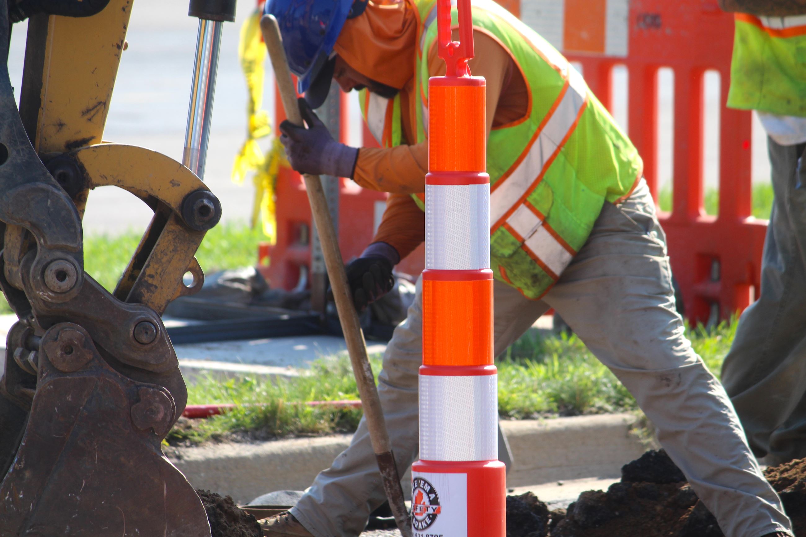 A man in safety gear works on a street under construction with a traffic cone nearby