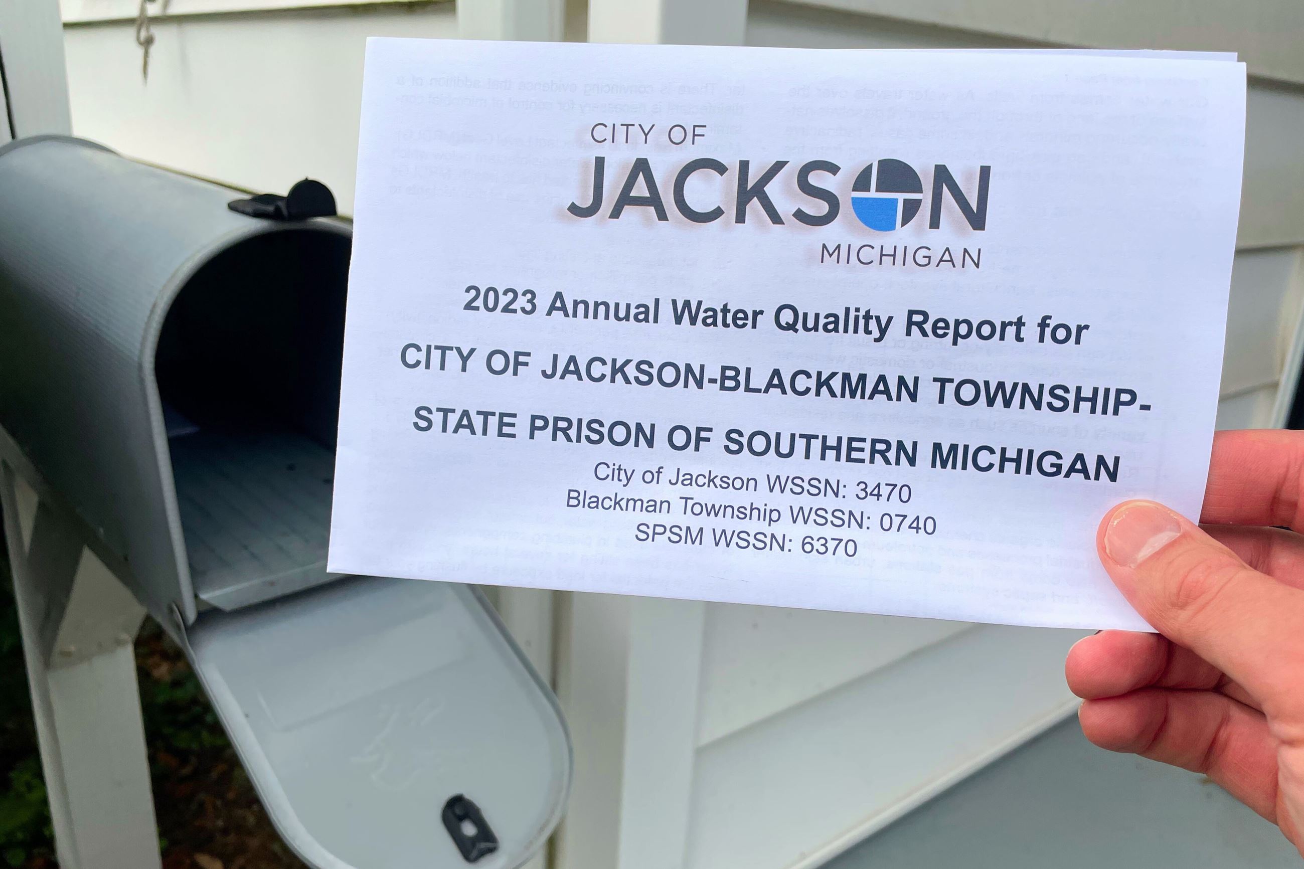 A hand holding a report about water in front of an open mailbox. 
