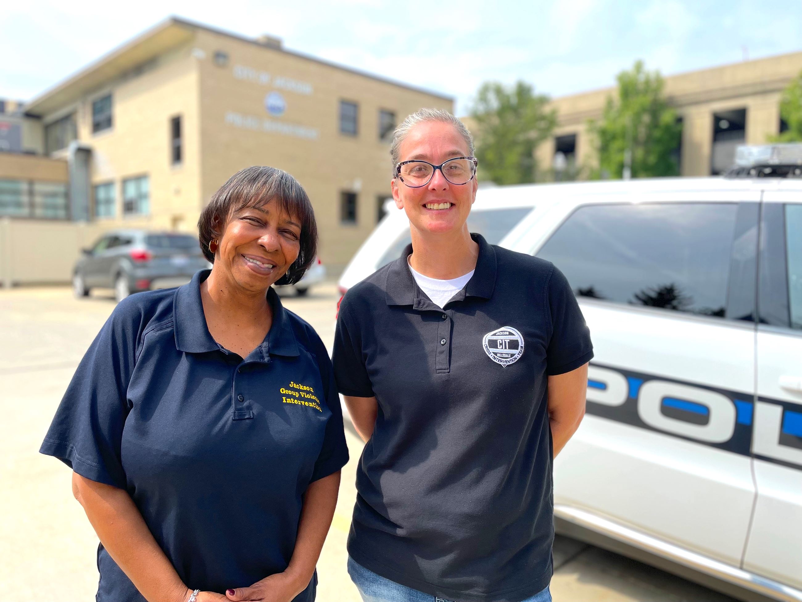 Two women pose next to a police patrol car 