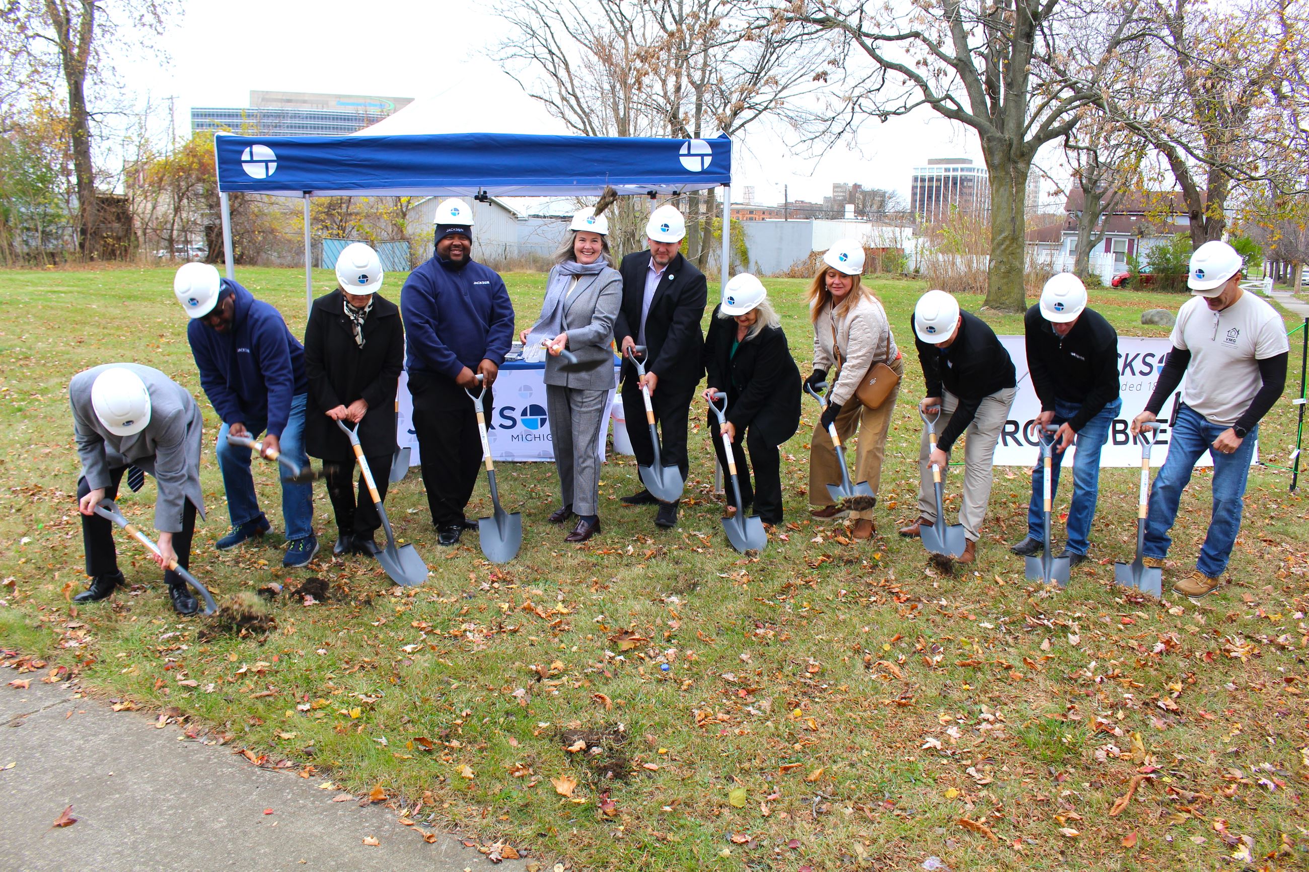 A group of men and women in hard hats dig into the ground with little shovels