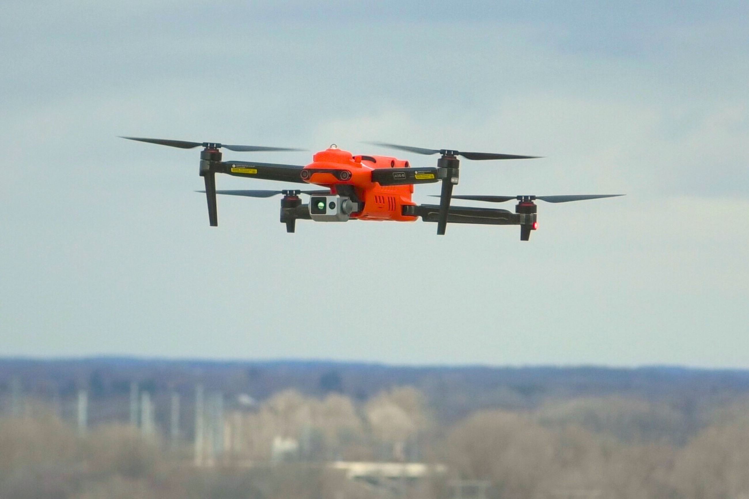 An orange drone flies through the sky