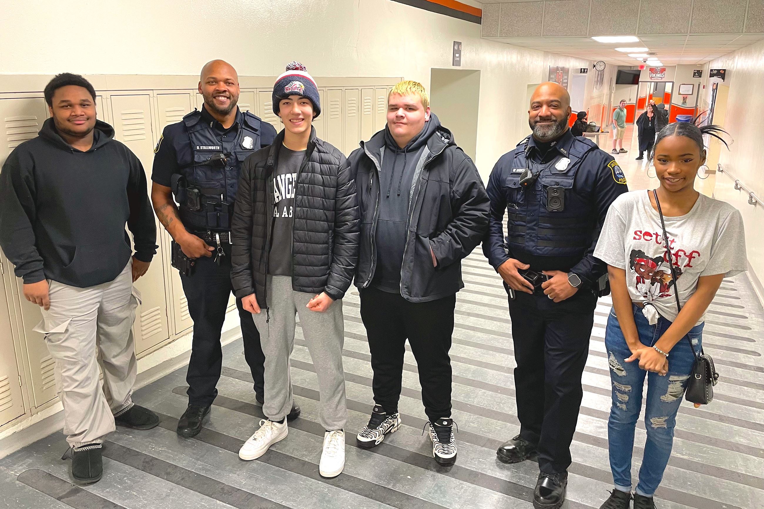 High school kids smile alongside police officers in a school hallway